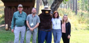 four people posing with smoky the bear in a forest