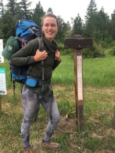 Kaili stands at a trailhead wearing a large backpack