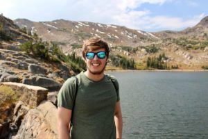 Travis smiles in front of an alpine lake