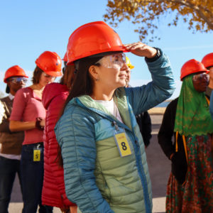 Carbon Management student looks toward the sun in a hard hat. She is with other students in a parking lot learning how to reduce emissions from a coal plant in Ecosystem Science and Sustainability class.