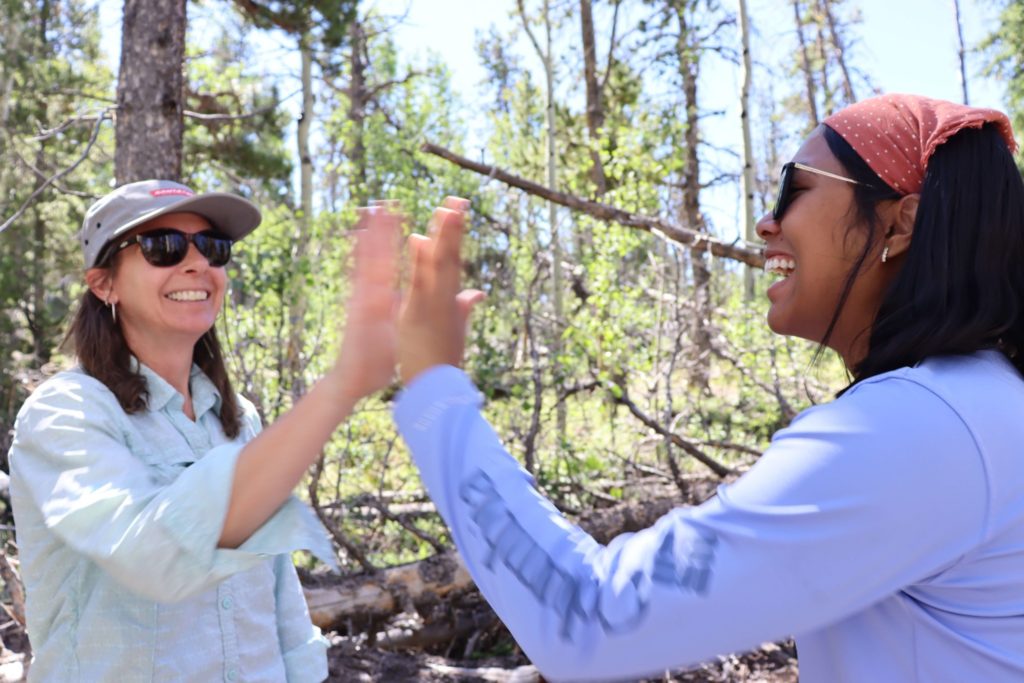 Two professional science master's of ecosystem science and sustainability students high five in the forest.