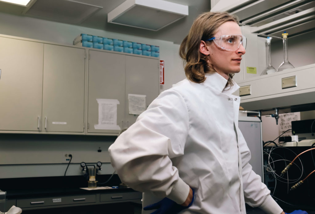 Student in lab coat and protective glasses contemplates his next move in the water science lab.