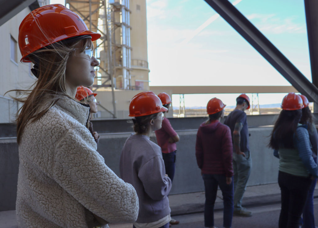 Students tour power plant looking toward the future, they are wearing orange hardhats.