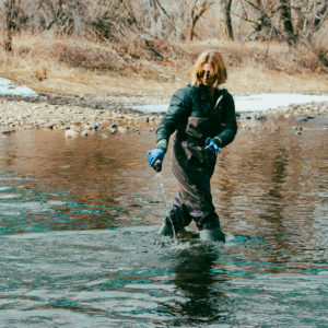 Woman takes samples in river for hydrologic analysis. She is standing in the river with waders.