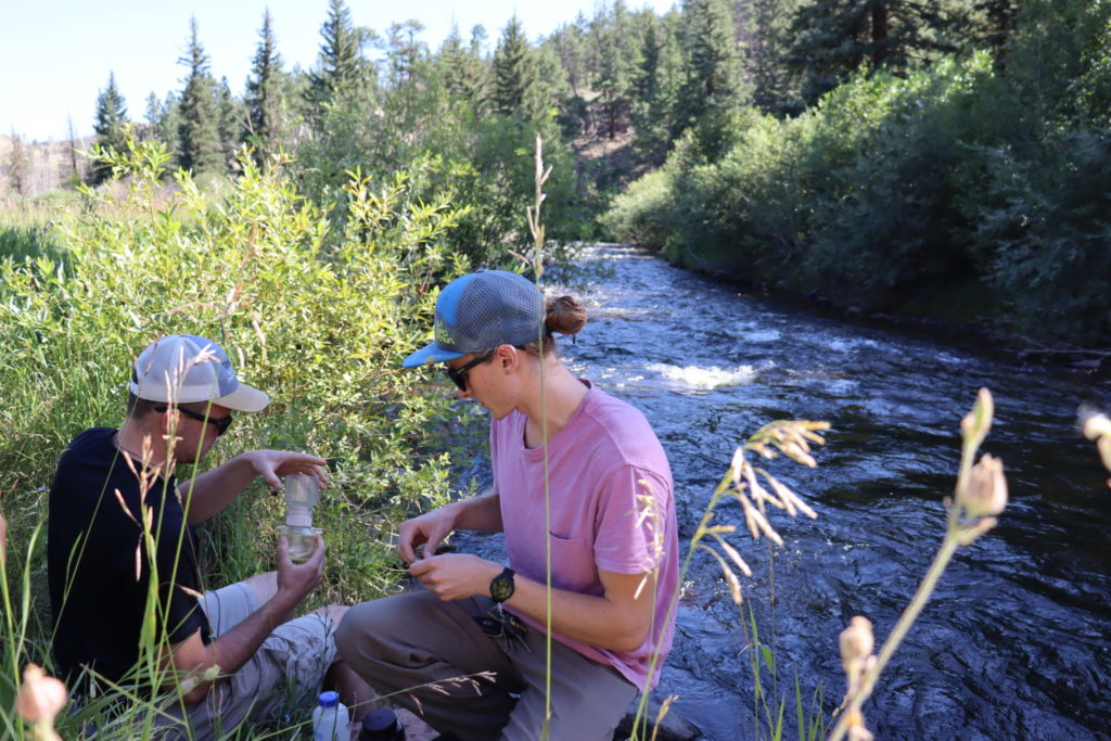 Two water resources graduate students take water quality samples by a river in Colorado.