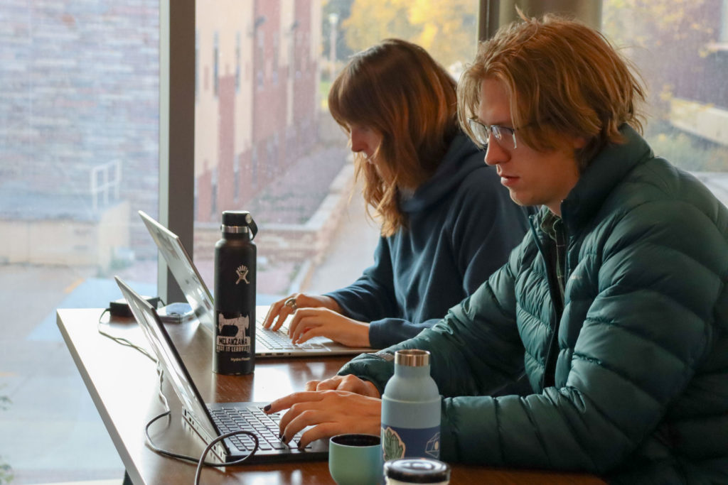 two students sit at computers near a window while studying data science