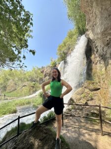 Melanie stands in front of a waterfall and smiles at camera