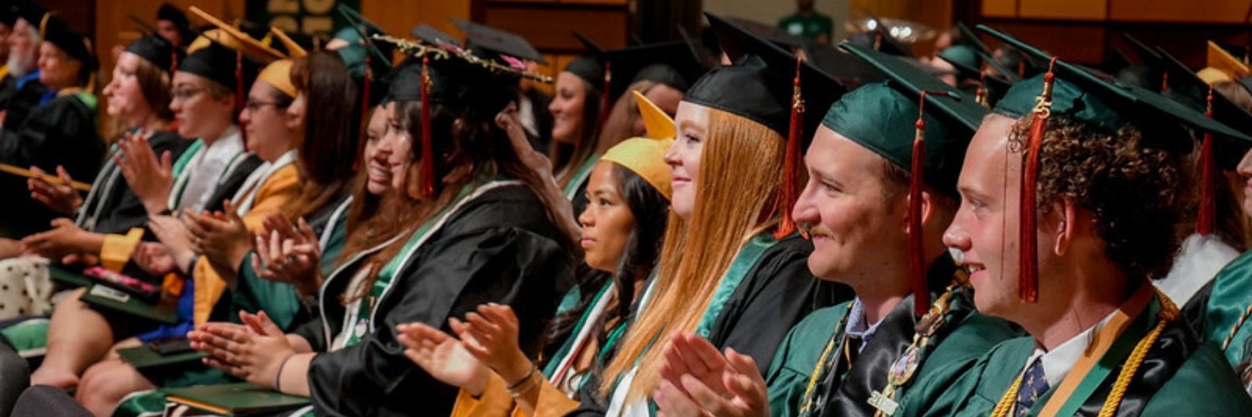 Graduates sit in a row clapping.
